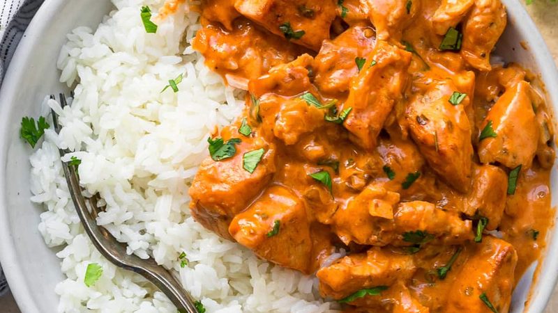 A bowl of chicken tikka masala with white rice and coriander